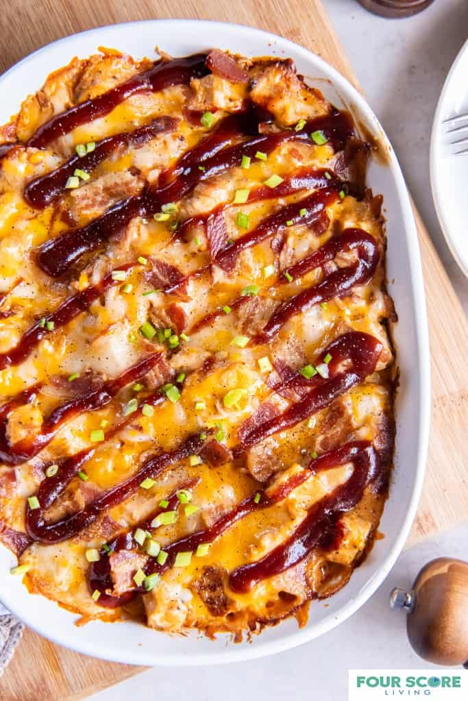 Aerial view of Keto BBQ Chicken Casserole in an oval white casserole placed on a light wood tone cutting board resting on a white stone surface.