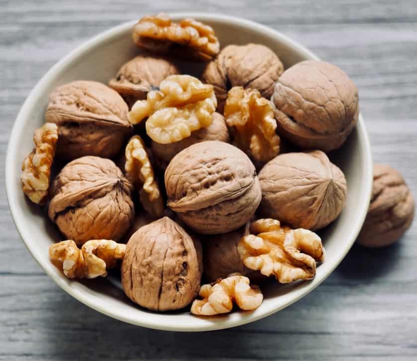 Closeup aerial view of a small white dish of walnut halves and walnuts in the shell resting on a wooden rustic background.