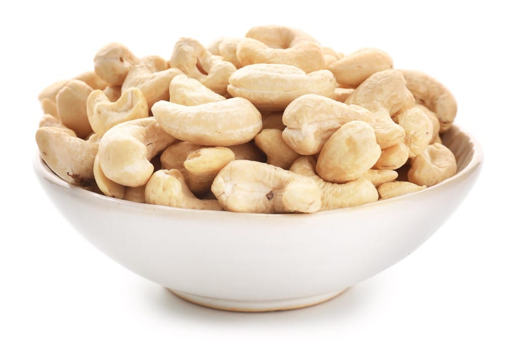 Front, closeup view of a white dish of raw cashews on a white background.
