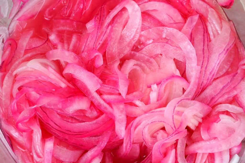 Close up aerial view of pickled onions with a pink/red coloring in a bowl.