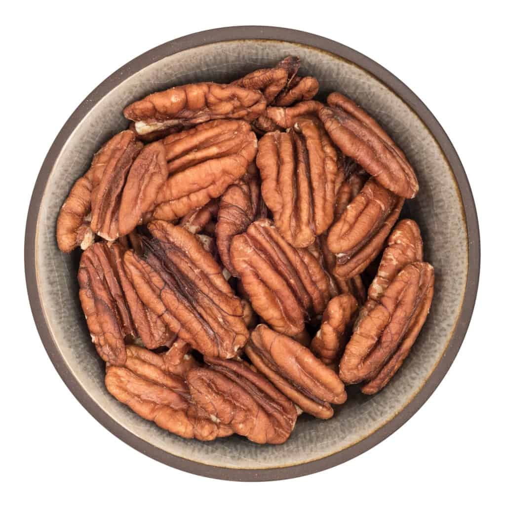 Two unshelled pecans, one with part of the shell removed exposing the flesh of the nut, one whole unshelled pecan and one pecan half with two small green leaves all on a white background.