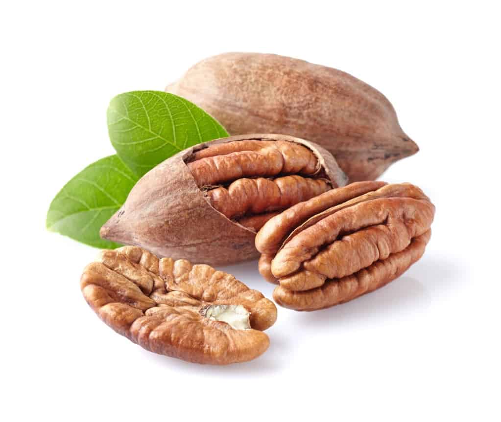 Two unshelled pecans, one with part of the shell removed exposing the flesh of the nut, one whole unshelled pecan and one pecan half with two small green leaves all on a white background.