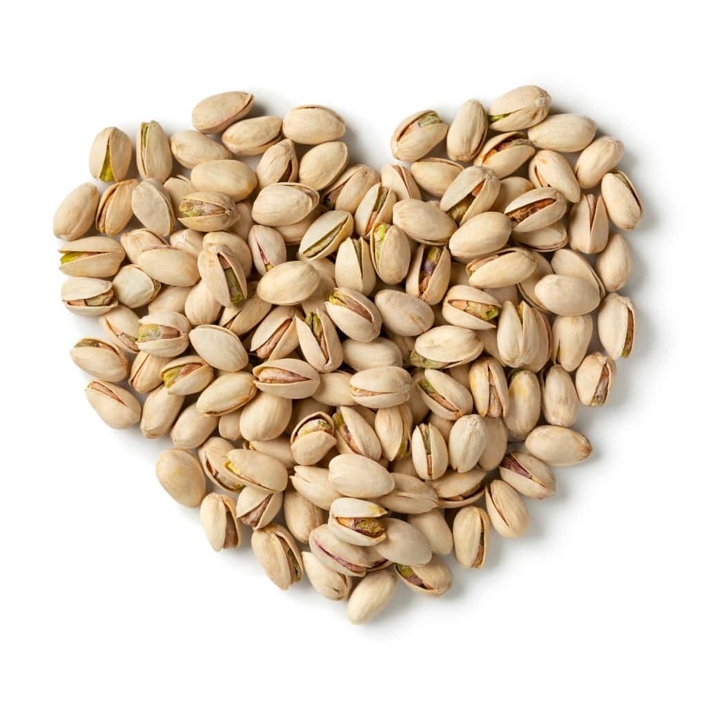 Aerial view of a pile of pistachio nuts with shells formed into a heart shape, on a white background.