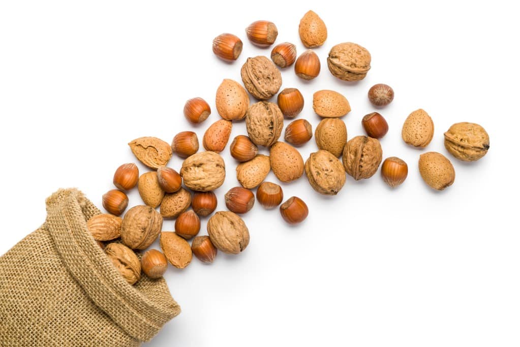 Aerial view of mix of nuts overflowing out of a small burlap bag and scattered onto a white background.