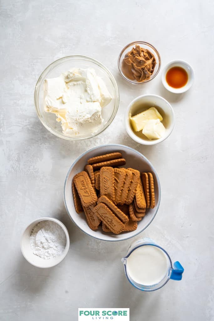 Aerial view of  various size bowls holding ingredients to make a Biscoff Cheesecake, including cream cheese,  Biscoff cookies, butter, Biscoff spread, heavy whipping cream, vanilla extract and  powdered sugar. 