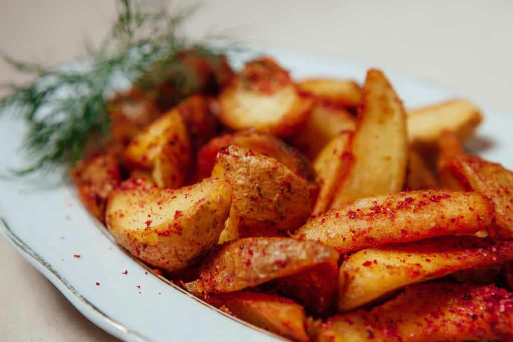 Close up diagonal view of jicama wedges with red seasoning on a white oval platter with a fresh green garnish in soft focus in the background.