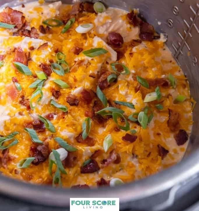 Up close view of diagonal aerial view of Instant Pot crack chicken topped with chopped bacon, shredded cheese and chopped green onions in an Instant Pot.