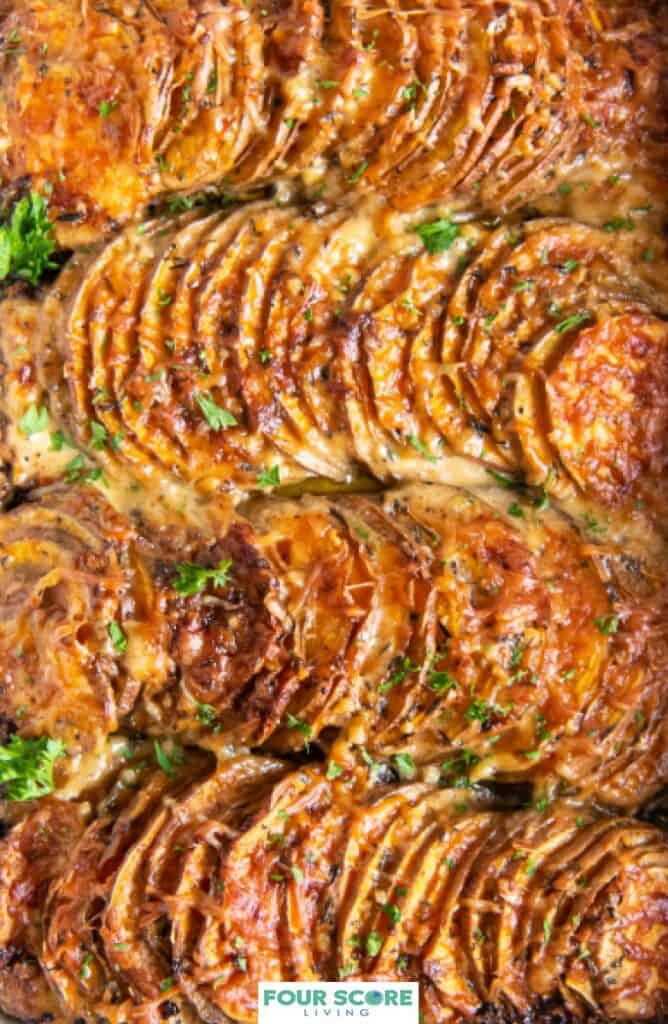 Extreme closeup view of scalloped sweet potatoes covered with cheese and sprinkled with finely chopped fresh green herbs filling the frame of the image.