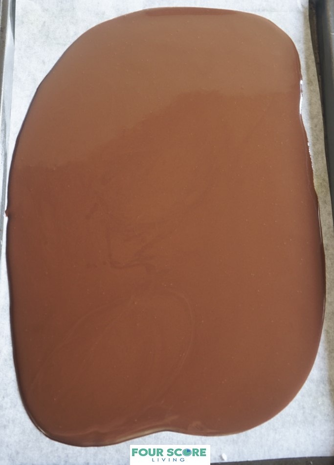 Aerial view of melted semisweet chocolate spread onto a parchment paper lined sheet pan.