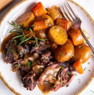 Up close aerial view of pot roast with onion soup mix with carrots and potatoes plated with a sprig of fresh rosemary.
