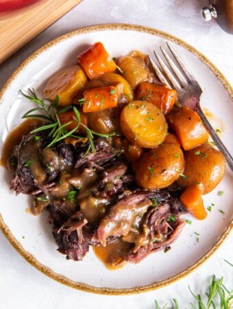 Up close aerial view of pot roast with onion soup mix with carrots and potatoes plated with a sprig of fresh rosemary.