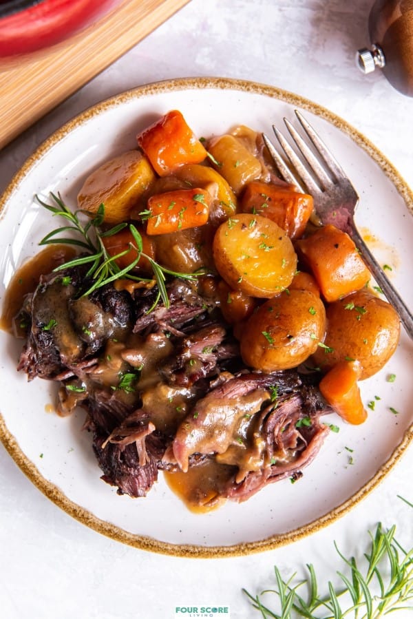 Up close aerial view of pot roast with onion soup mix with carrots and potatoes plated with a sprig of fresh rosemary. 