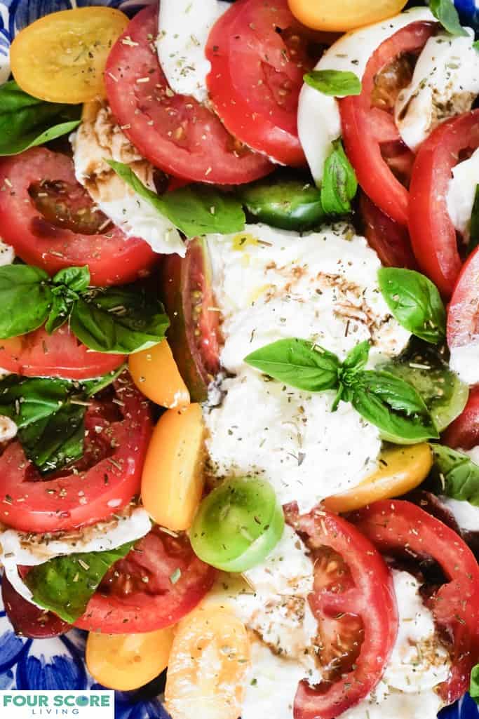 Close up aerial view of prepared burrata caprese dish with yellow and red tomatoes, burrata cheese, fresh basil with drizzled balsamic vinegar and sprinkled with dry herbs.